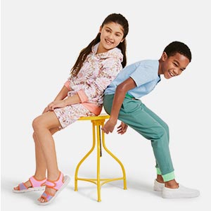 Two children smile while both try to fit on the same stool.