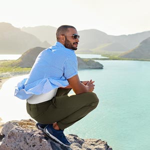 A man crouches on some rocks, enjoying the view of a body of water.